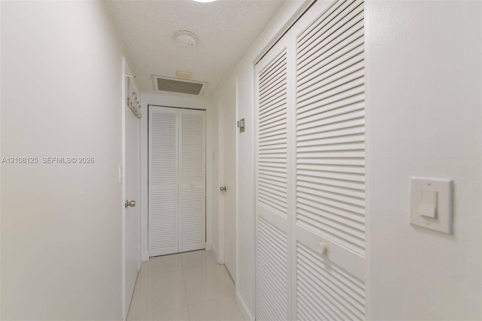 1985 S Ocean Drive, #8M, Hallandale Beach, FL 33009 Hallway featuring high-gloss tile flooring, white-painted walls, and dual sets of white louvered-panel closet doors