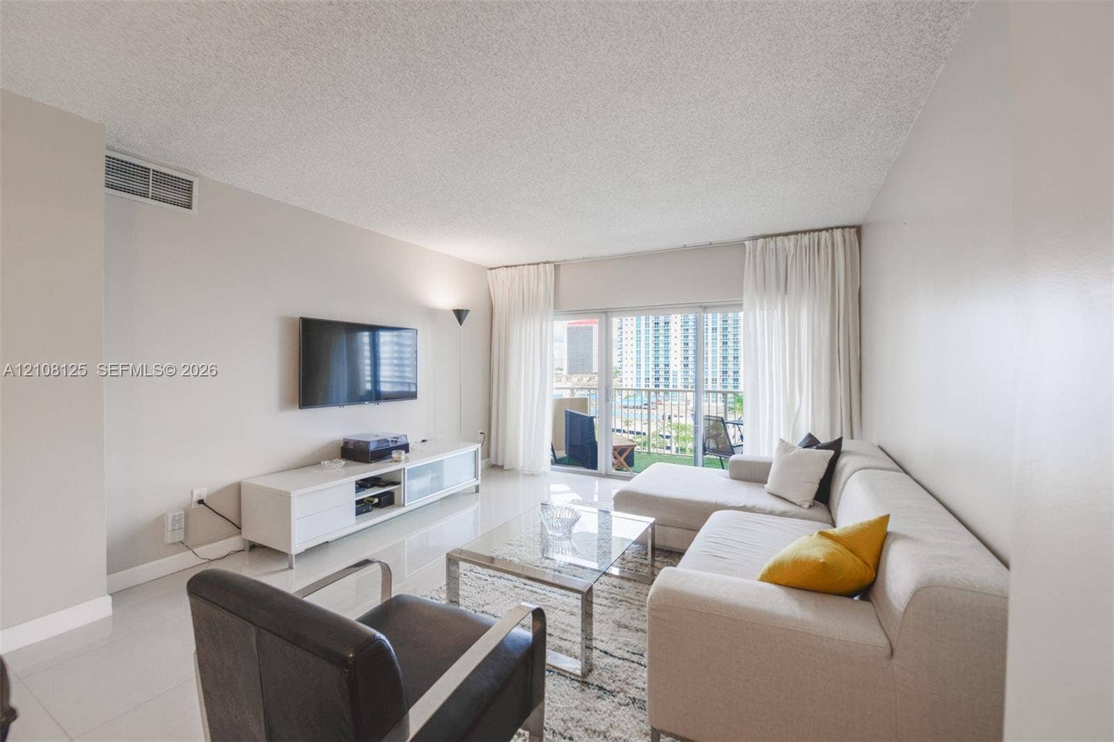1985 S Ocean Drive, #8M, Hallandale Beach, FL 33009 Living area featuring large-format tile flooring, textured ceiling, and sliding glass doors with access to a private balcony