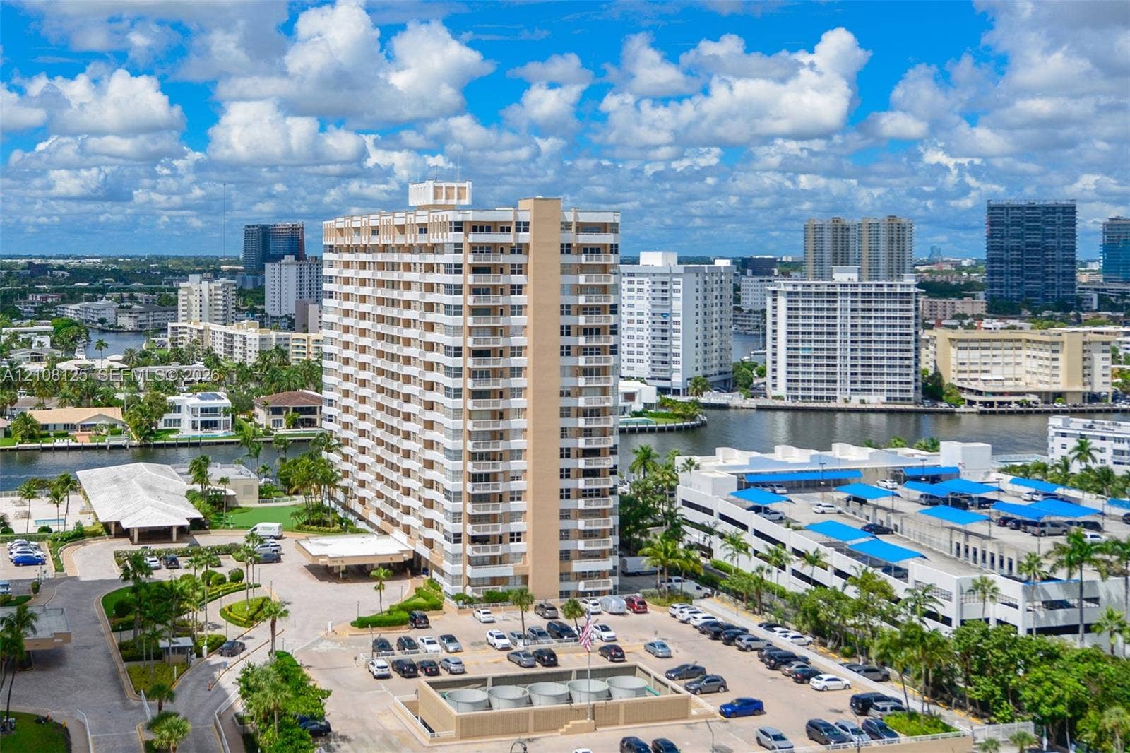 1985 S Ocean Drive, #8M, Hallandale Beach, FL 33009 High-rise residential building featuring private balconies, expansive surface parking, a porte-cochre entry, and landscaped grounds set against a waterfront backdrop