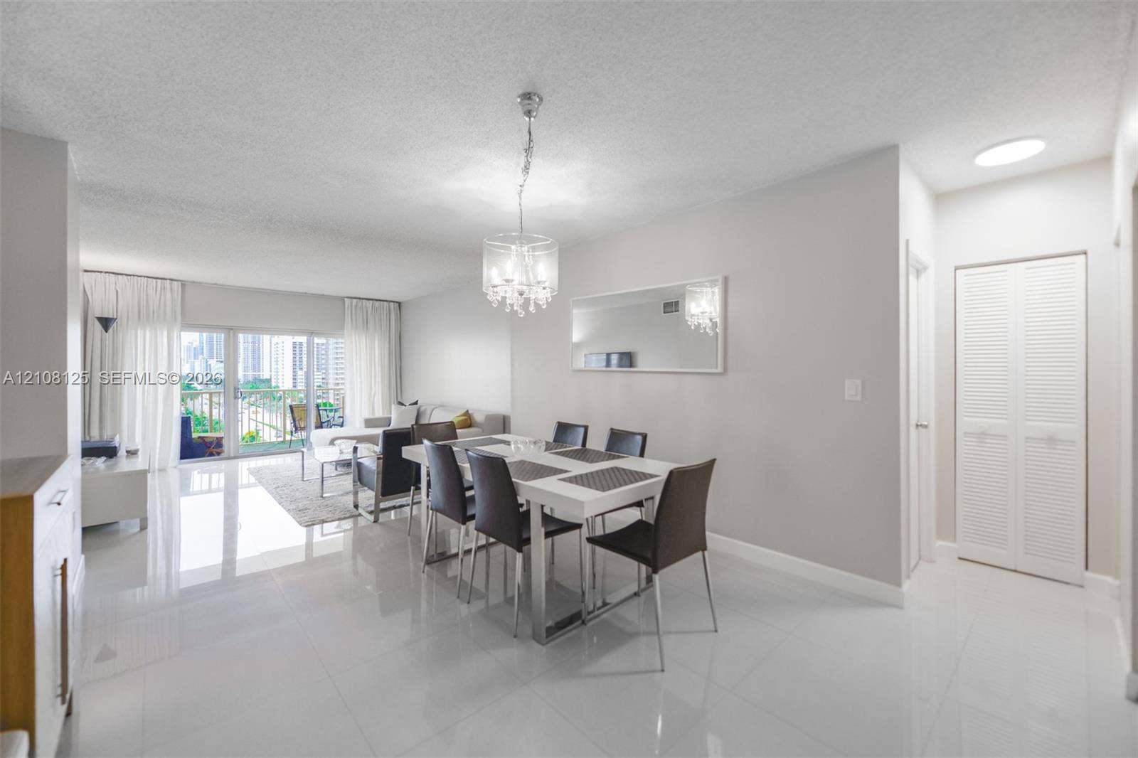 1985 S Ocean Drive, #8M, Hallandale Beach, FL 33009 Open-concept living space featuring high-gloss tile flooring, an ornate crystal chandelier, a large wall-mounted mirror, and white louvered-panel closet doors