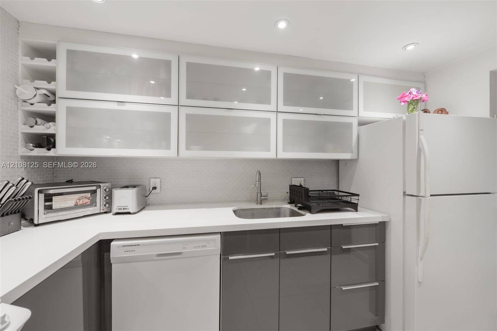 1985 S Ocean Drive, #8M, Hallandale Beach, FL 33009 Kitchen featuring high-gloss charcoal base cabinetry, upper cabinets with frosted glass inserts, solid-surface countertops, recessed ceiling lighting, and integrated wine storage