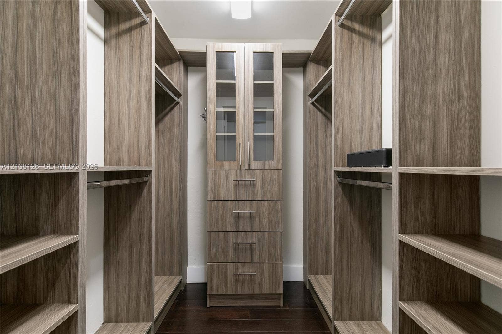 11700 NW 4th Street, Plantation, Plantation, FL 33325 Custom walk-in closet featuring extensive wood-finish shelving, integrated hanging rods, a central stack of four soft-close drawers, and upper cabinetry with glass-panel doors