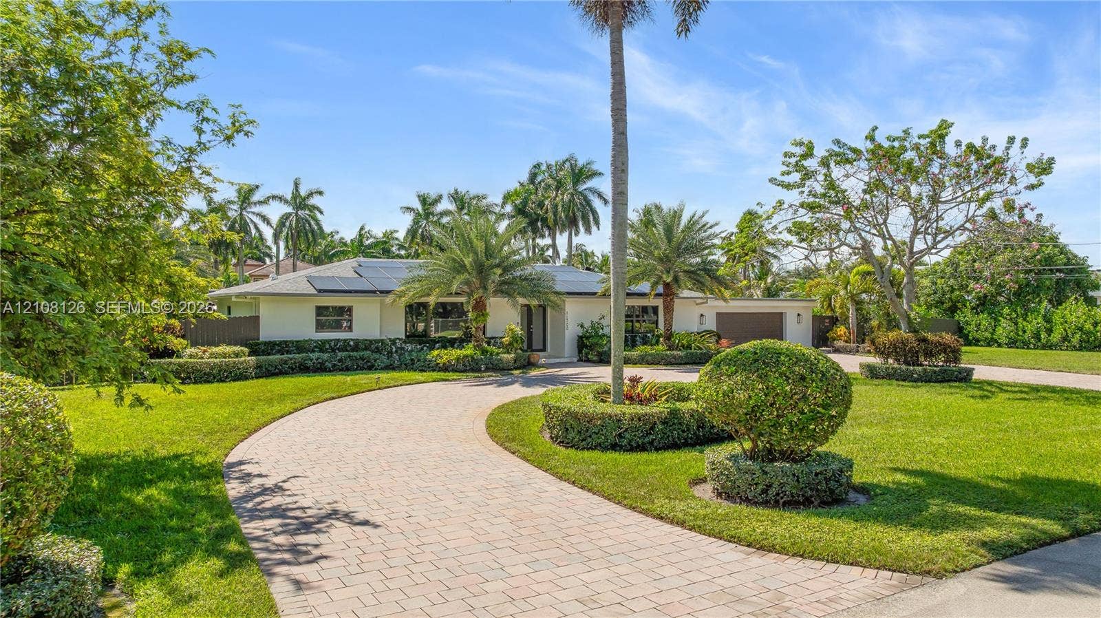11700 NW 4th Street, Plantation, Plantation, FL 33325 Single-story exterior featuring a paver circular driveway, solar panel installation, manicured landscaping with mature palm trees, and an attached two-car garage