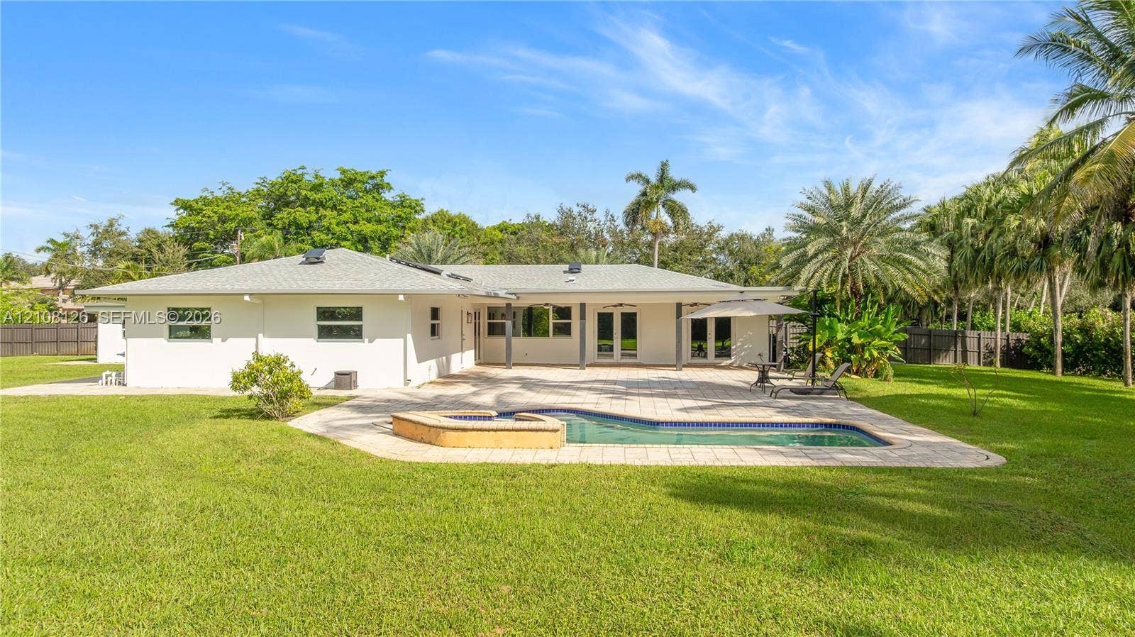 11700 NW 4th Street, Plantation, Plantation, FL 33325 Rear exterior featuring a paver patio, in-ground pool with a raised stone-finish spillway, expansive grass lawn, and mature perimeter landscaping
