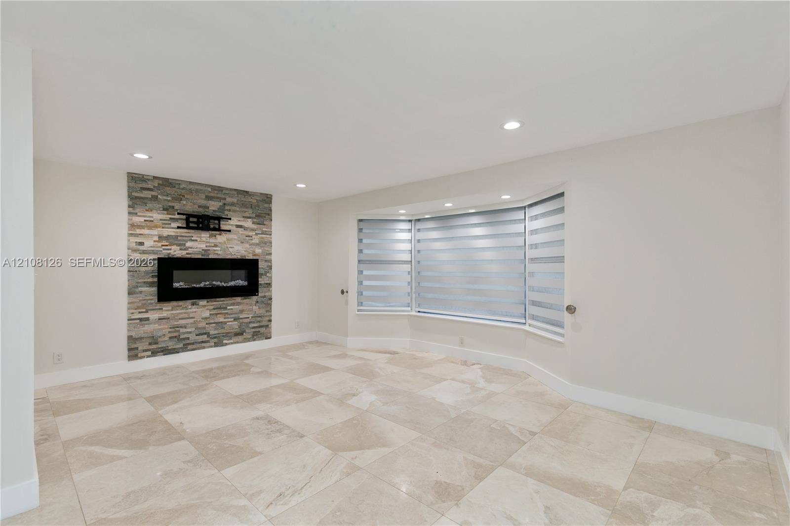 11700 NW 4th Street, Plantation, Plantation, FL 33325 Stone-accented fireplace with a wall-mounted fire feature, large bay window, and light-toned tile flooring