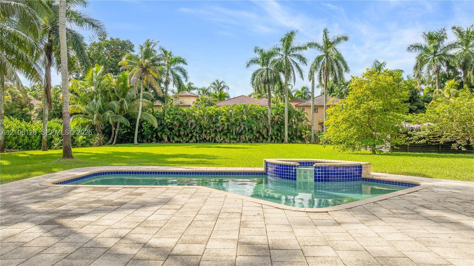 11700 NW 4th Street, Plantation, Plantation, FL 33325 In-ground swimming pool with an attached spillover spa, blue tile detailing, expansive paver patio, and mature palm trees set against a private lawn