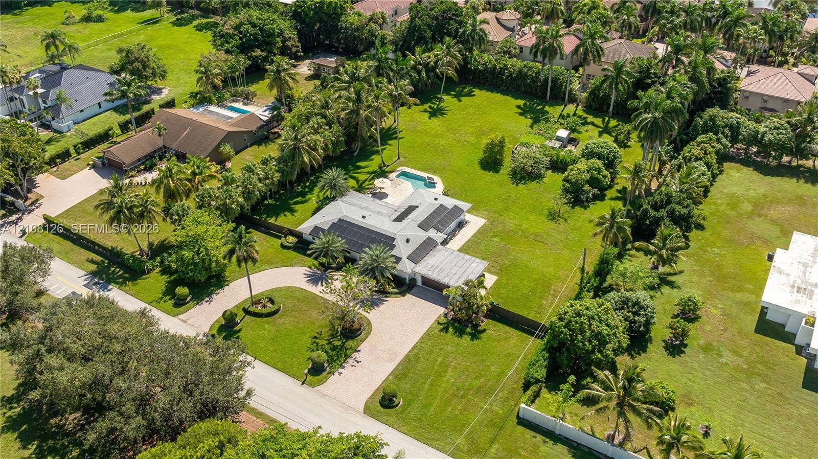 11700 NW 4th Street, Plantation, Plantation, FL 33325 Aerial perspective of an expansive lot featuring a multi-gabled residence, a paved circular driveway, a private in-ground swimming pool, and solar panel arrays