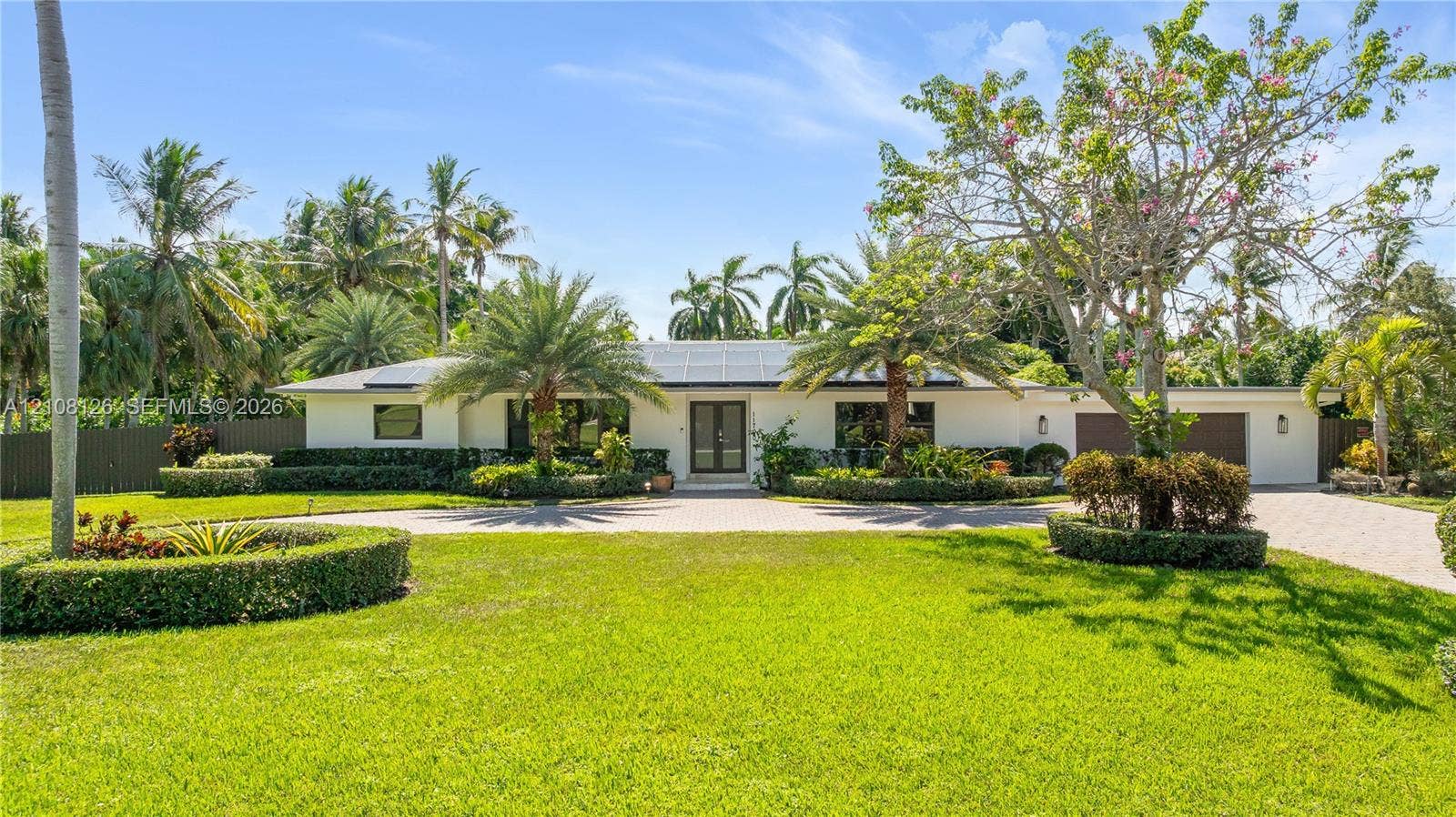 11700 NW 4th Street, Plantation, Plantation, FL 33325 Single-story exterior featuring a light-toned stucco faade, solar panels, paver driveway, manicured landscaping, and mature palm trees