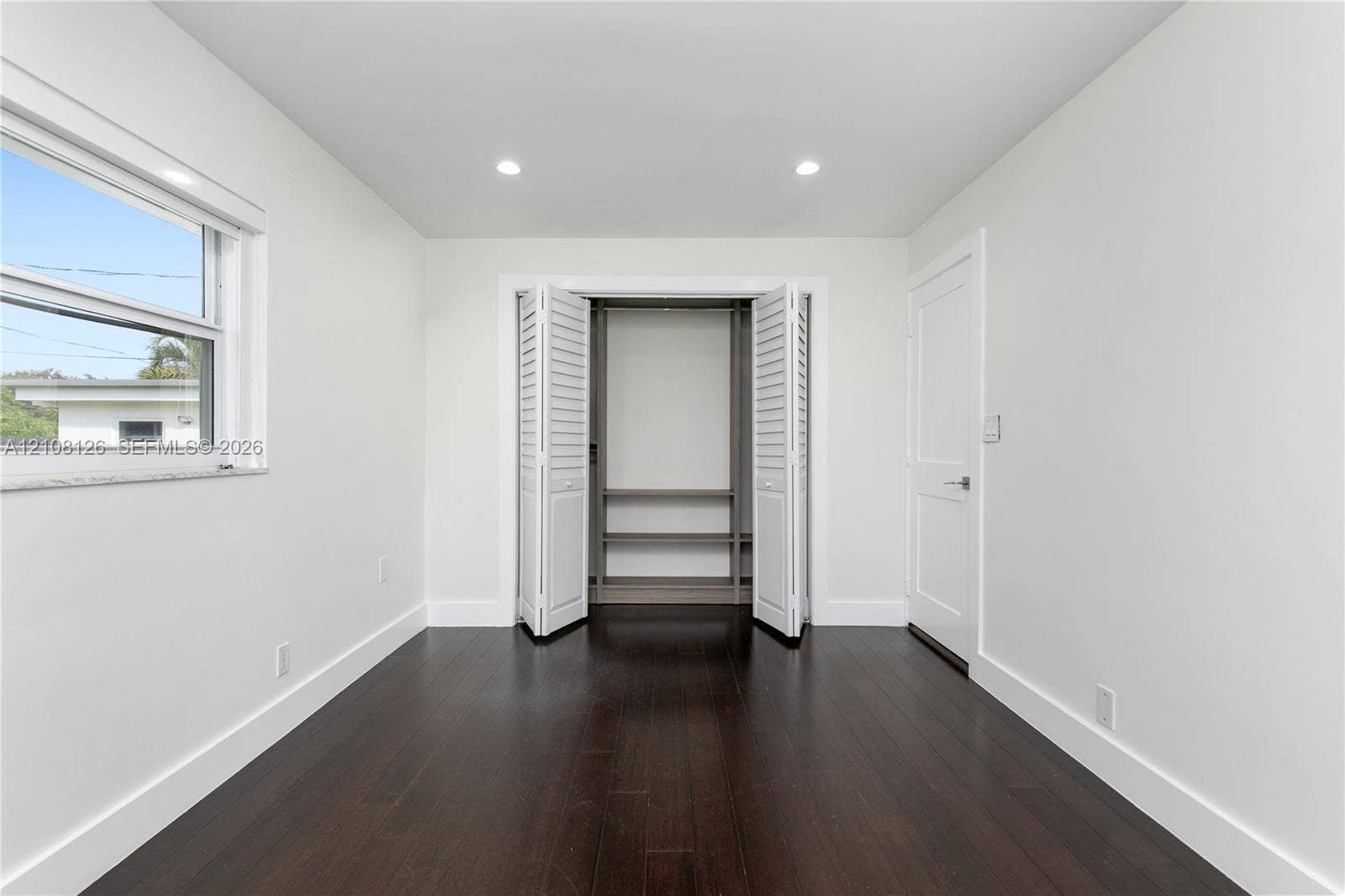 11700 NW 4th Street, Plantation, Plantation, FL 33325 Interior room featuring wood-finish flooring, recessed lighting, white walls, louvered closet doors with built-in shelving, and a dual-pane window