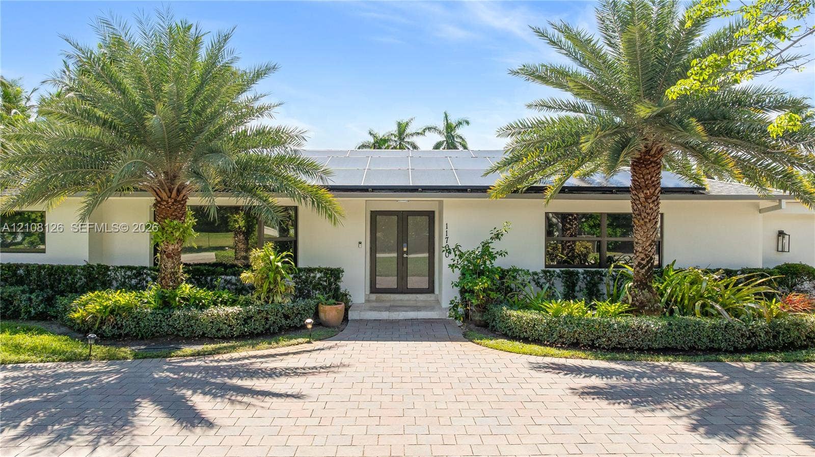 11700 NW 4th Street, Plantation, Plantation, FL 33325 Exterior facade featuring a paved stone driveway, double-door entrance, integrated solar panels, and mature palm trees
