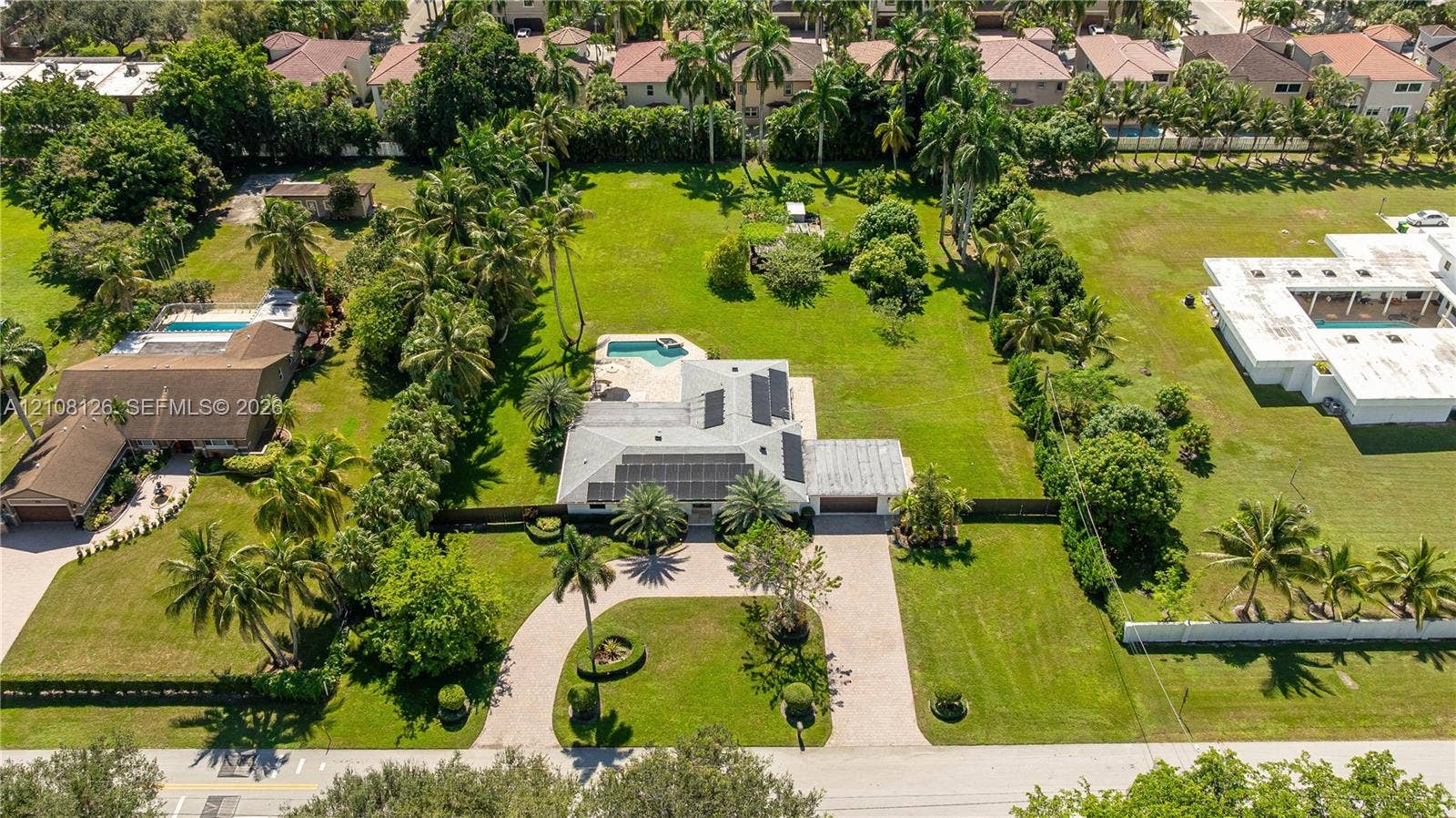 11700 NW 4th Street, Plantation, Plantation, FL 33325 Expansive lot featuring a circular paver driveway, mature landscaping, roof-mounted solar panels, and an in-ground swimming pool