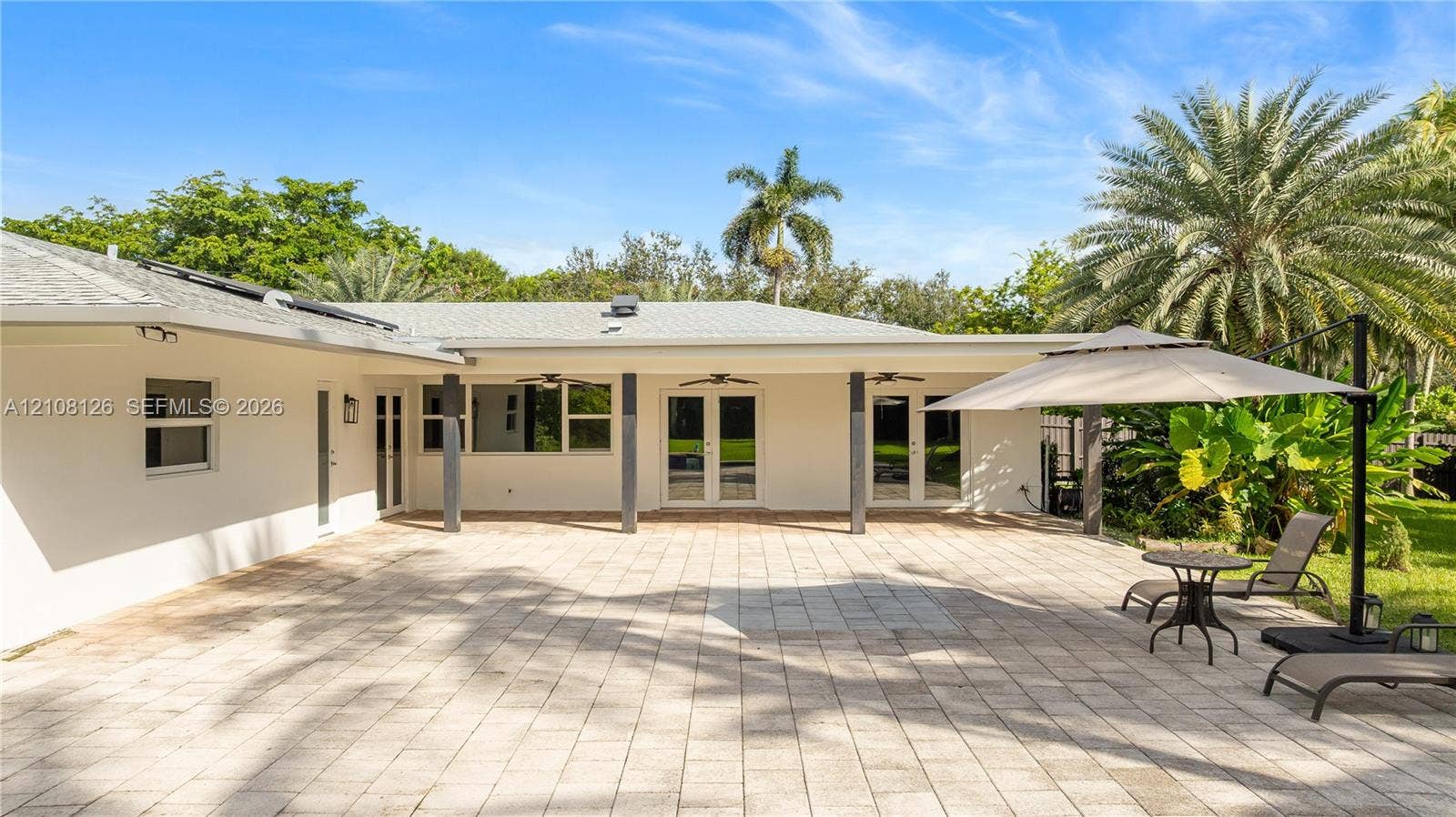 11700 NW 4th Street, Plantation, Plantation, FL 33325 Expansive paver patio featuring a covered area with ceiling fans, dual French door entries, and mature landscaping