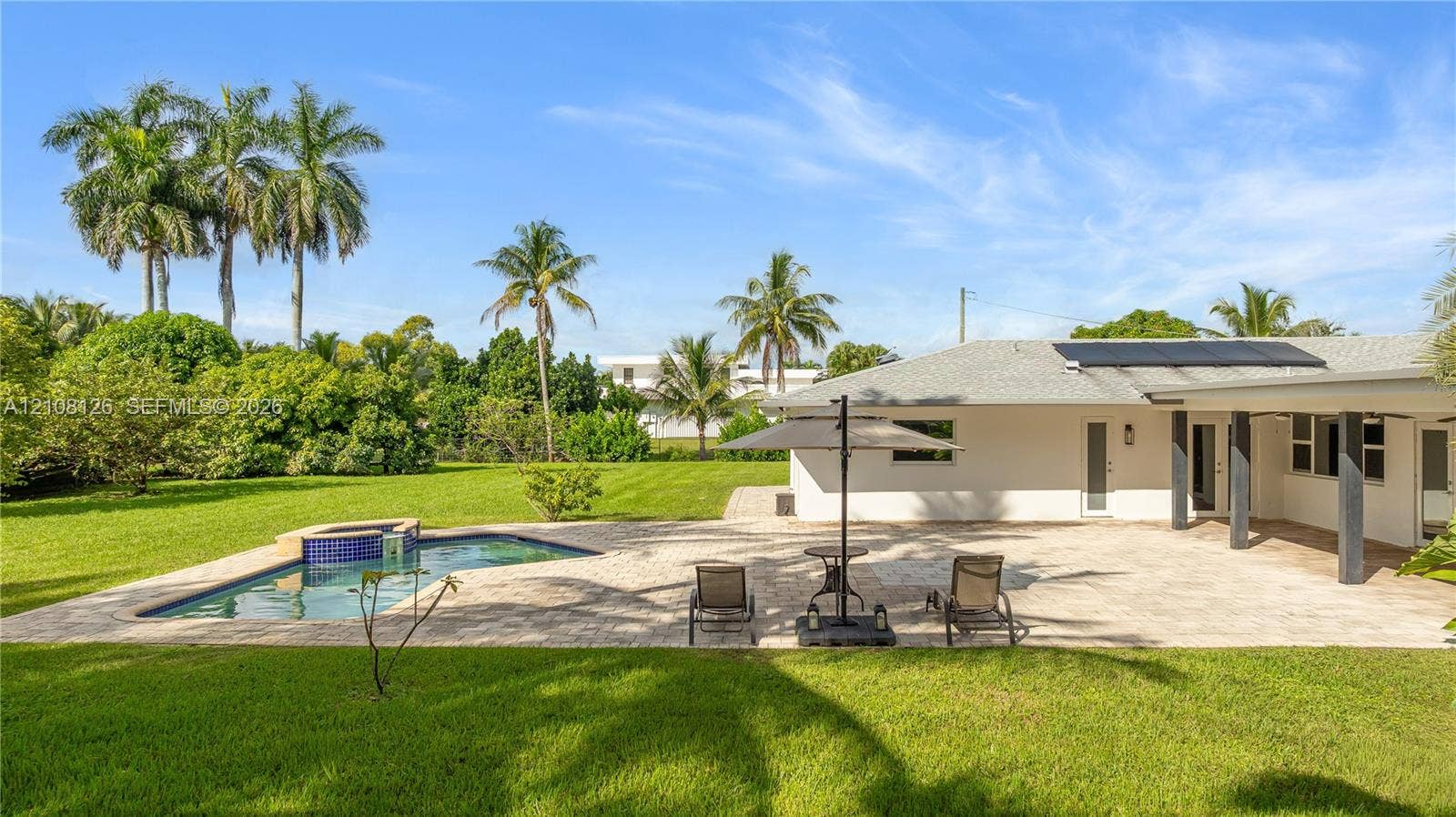 11700 NW 4th Street, Plantation, Plantation, FL 33325 Expansive backyard featuring a stone-paved patio, custom swimming pool with built-in spa, solar panel roof installation, and mature landscaping