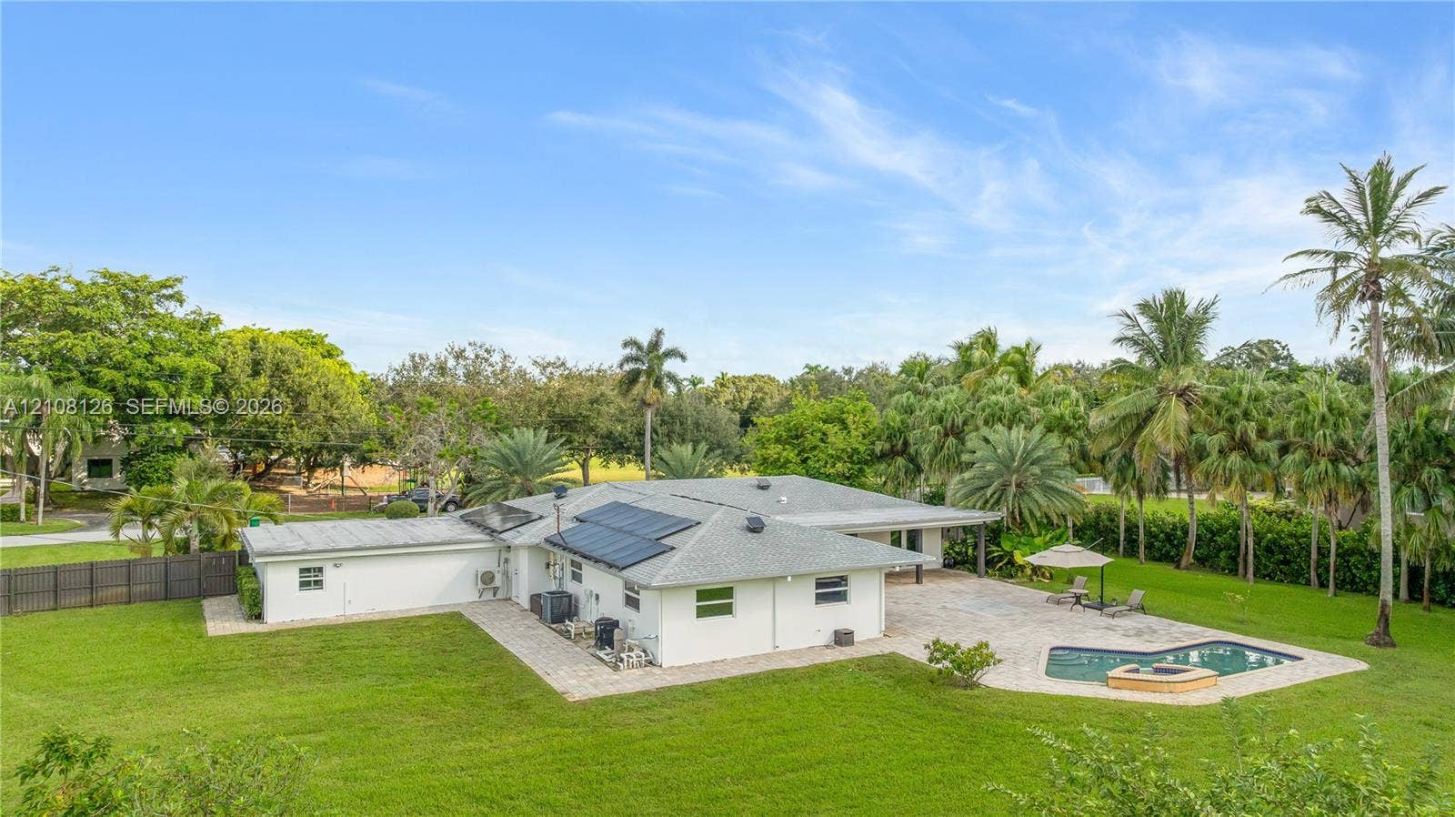11700 NW 4th Street, Plantation, Plantation, FL 33325 Expansive backyard featuring a paver patio, in-ground pool with a spillover spa, solar panel array, and mature landscaping