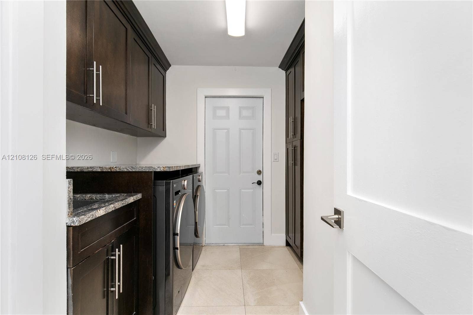 11700 NW 4th Street, Plantation, Plantation, FL 33325 Dark-finish cabinetry with silver-tone hardware, stone-composite countertops, built-in tall pantry storage, and light-tone tile flooring