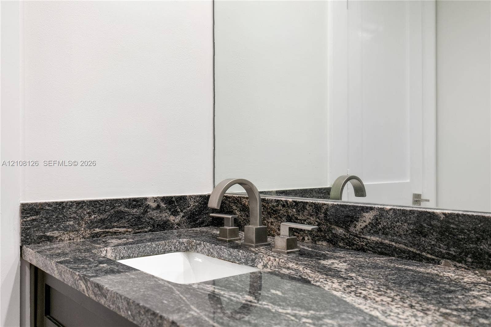 11700 NW 4th Street, Plantation, Plantation, FL 33325 Stone countertop with integrated backsplash, under-mount basin, and metallic widespread faucet, complemented by a wall-mounted mirror