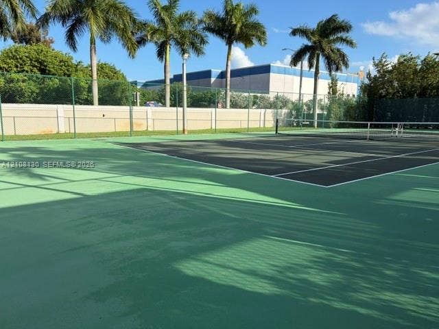 Tennis court featuring a hard surface, perimeter chain-link fencing, a center net, and mature palm trees