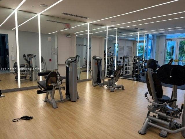 Fitness center featuring wood-finish flooring, floor-to-ceiling mirrored walls, and recessed linear lighting