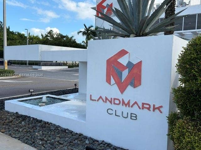 Landmark Club monument signage featuring white concrete masonry, decorative stone hardscaping, an integrated water fountain, and ornamental agave plants