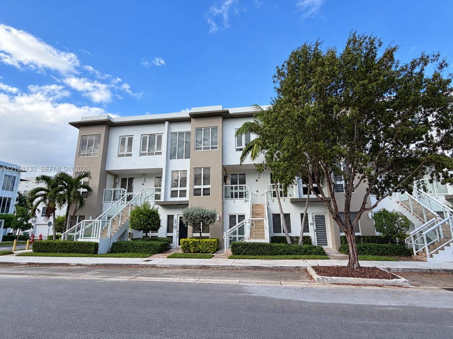 Three-story contemporary townhouse exterior featuring multi-pane windows, glass-panel railings, external staircases, and manicured landscaping