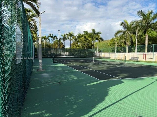 Tennis court with a multi-colored hard surface, perimeter chain-link fencing, and surrounding palm trees