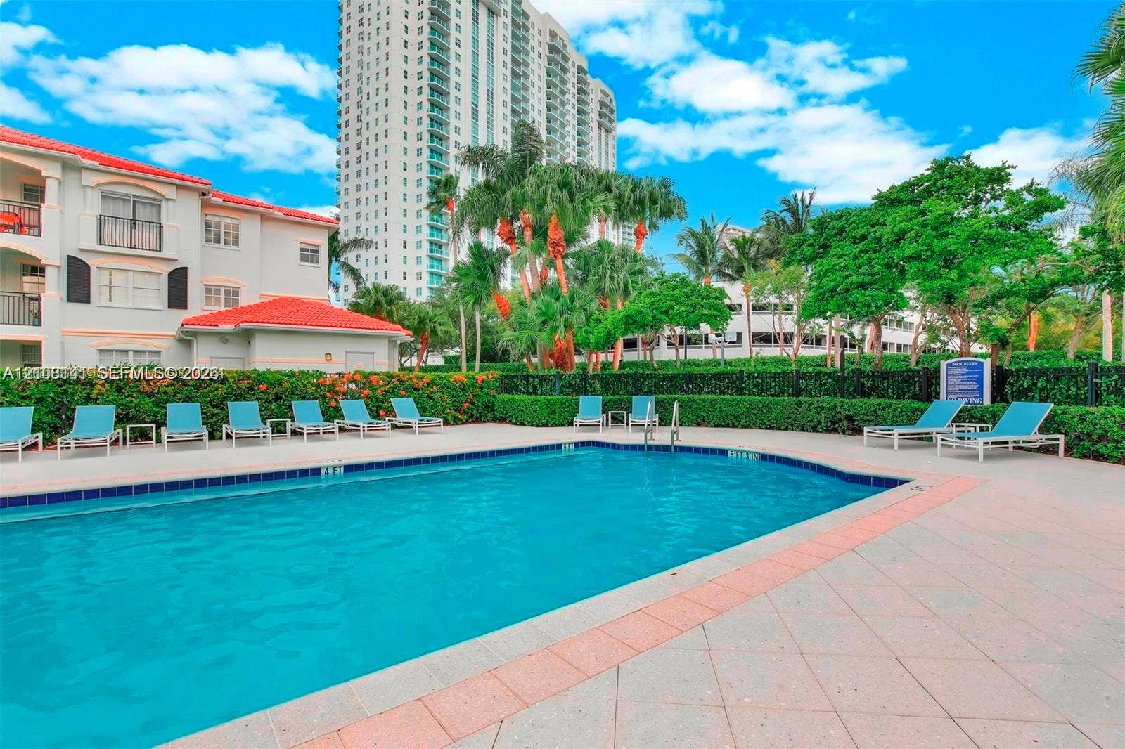 3135 NE 184th Street, #2205, Aventura, FL 33160 Outdoor swimming pool featuring a tiled deck, perimeter hedge landscaping, and metal fencing