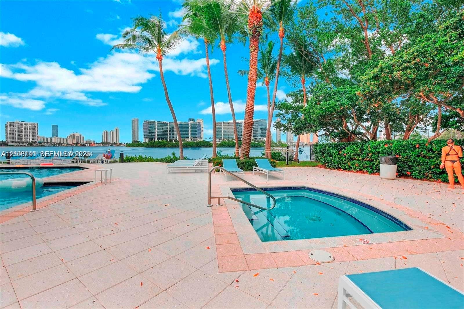 3135 NE 184th Street, #2205, Aventura, FL 33160 Waterfront pool and spa area featuring paved decking, mature palm trees, and metallic safety railings