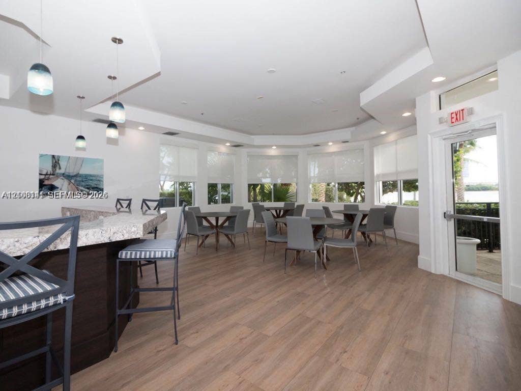 3135 NE 184th Street, #2205, Aventura, FL 33160 Multipurpose room featuring wood-finish flooring, a built-in bar with stone countertop, multi-tier recessed ceiling, and floor-to-ceiling windows with roller shades