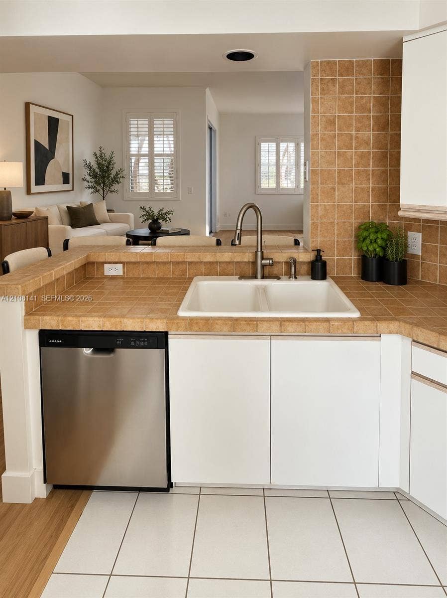 3135 NE 184th Street, #2205, Aventura, FL 33160 Kitchen area featuring a stainless steel dishwasher, white cabinetry, tiled countertops and backsplash, and a dual-basin sink with a gooseneck faucet