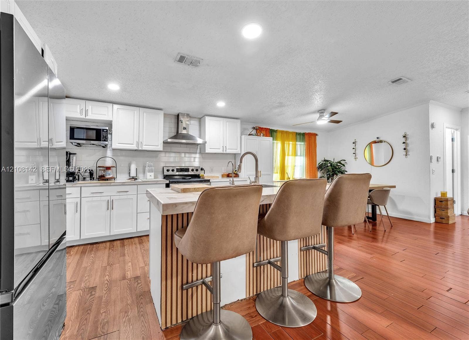 Kitchen featuring white cabinetry, wood-finish flooring, a central island with vertical wood-slat detailing, a stainless steel range hood, and recessed lighting