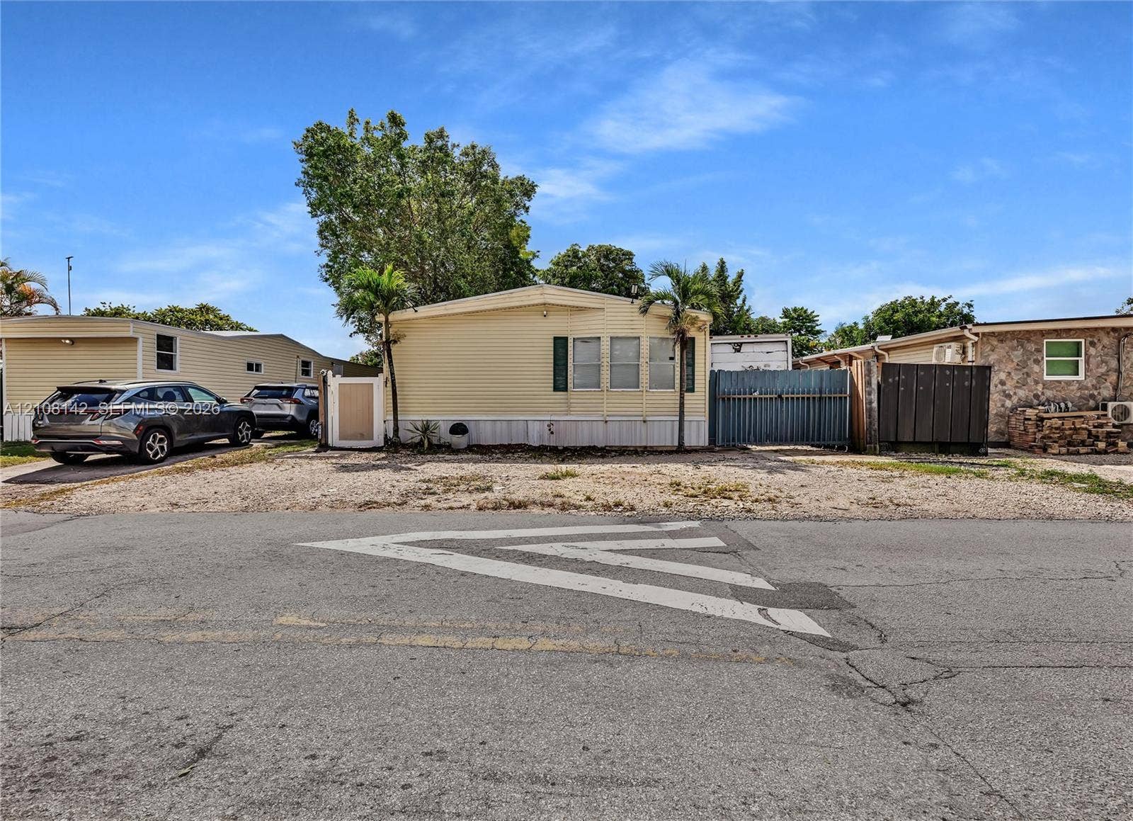 Exterior featuring light-colored horizontal siding, dual palm trees, and gravel ground cover