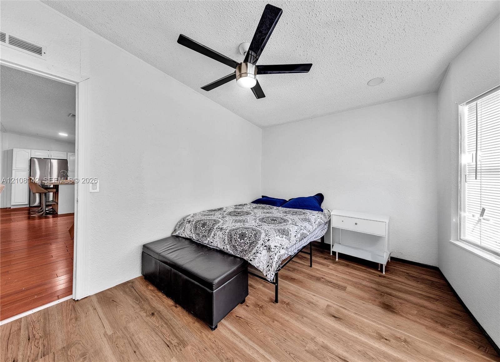 Room featuring wood-finish flooring, a matte black five-blade ceiling fan with integrated lighting, and horizontal window blinds