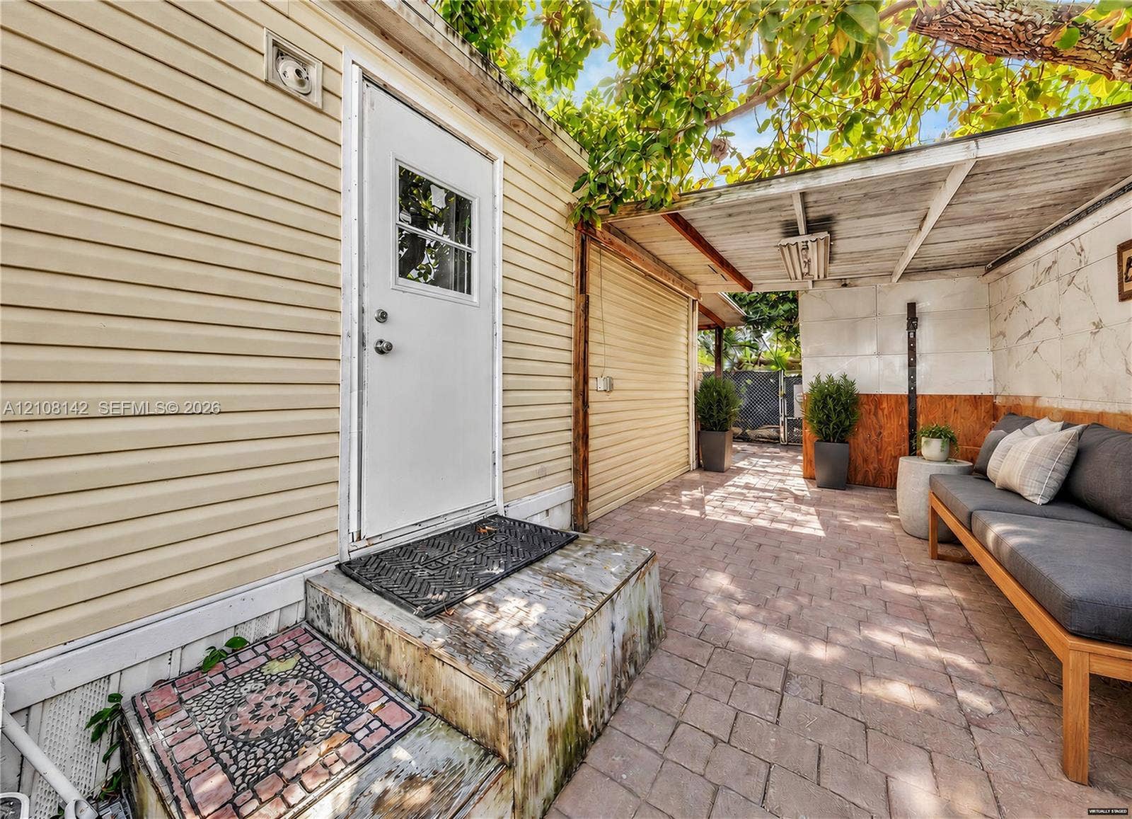 Exterior space featuring light-toned horizontal siding, a covered patio area with a paved surface, and an attached side structure