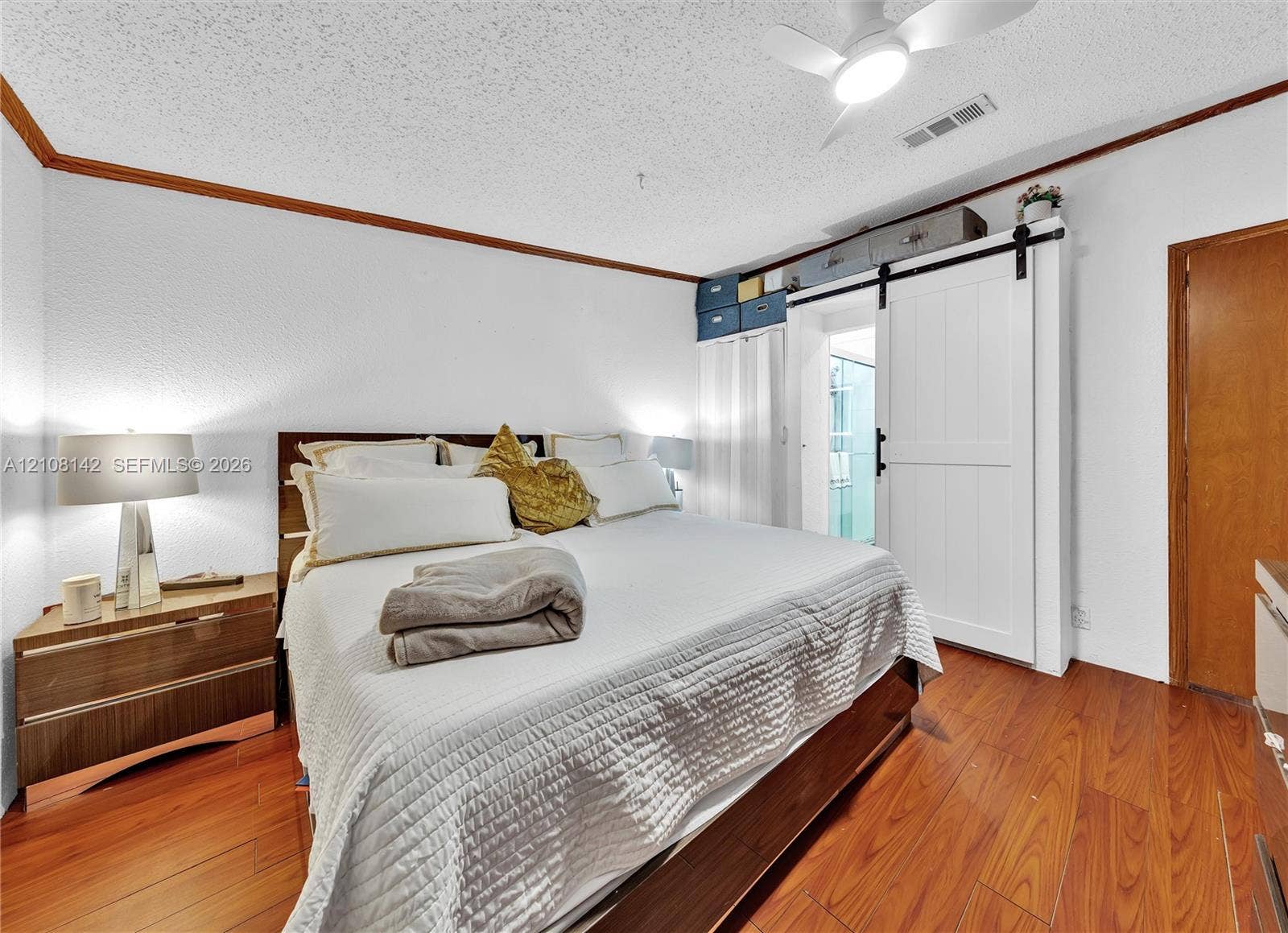Wood-finish flooring, white sliding barn door with black hardware, and ceiling-mounted fan with integrated light