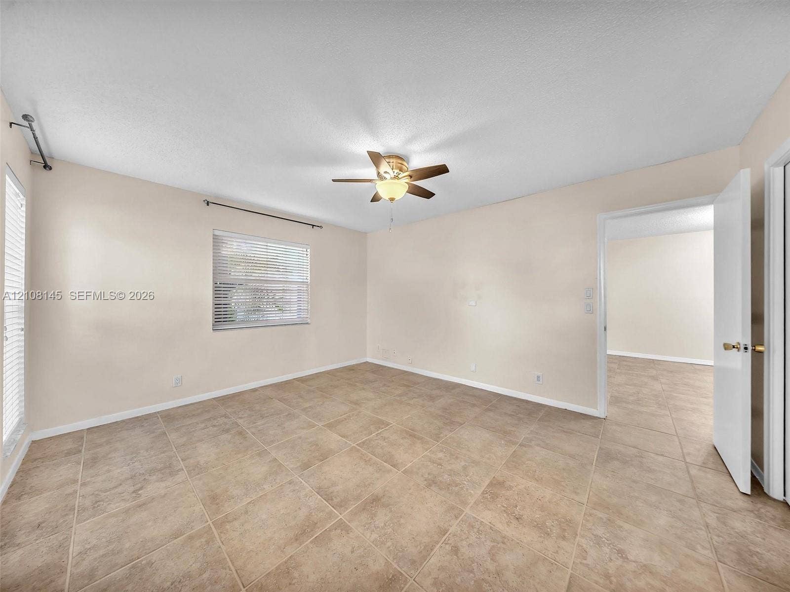 1020 Citrus Way, #101, Delray Beach, FL 33445 Neutral-toned interior space featuring large-format stone-style tile flooring, dual windows with horizontal blinds, and a central ceiling fan with integrated light fixture
