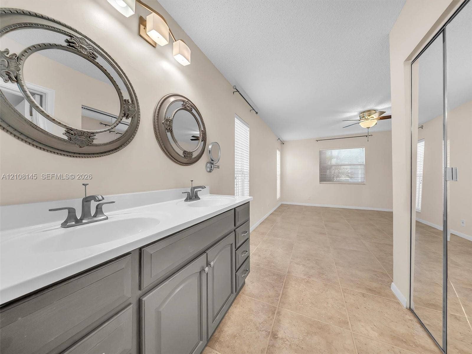 1020 Citrus Way, #101, Delray Beach, FL 33445 Dual-sink vanity with gray cabinetry and white countertop, ceramic tile flooring, ceiling fan, and mirrored closet doors