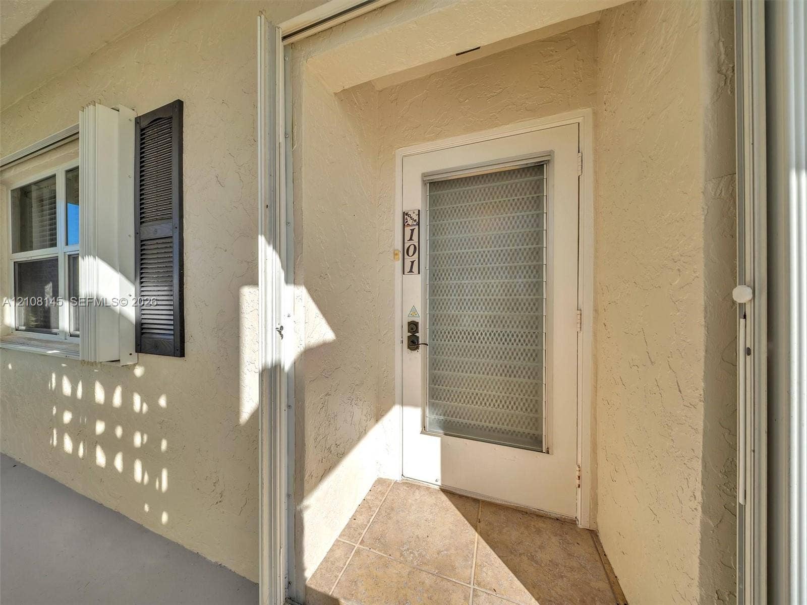 1020 Citrus Way, #101, Delray Beach, FL 33445 Exterior entry featuring stucco finish, louvered shutters, tile flooring, and a glass-paneled storm door