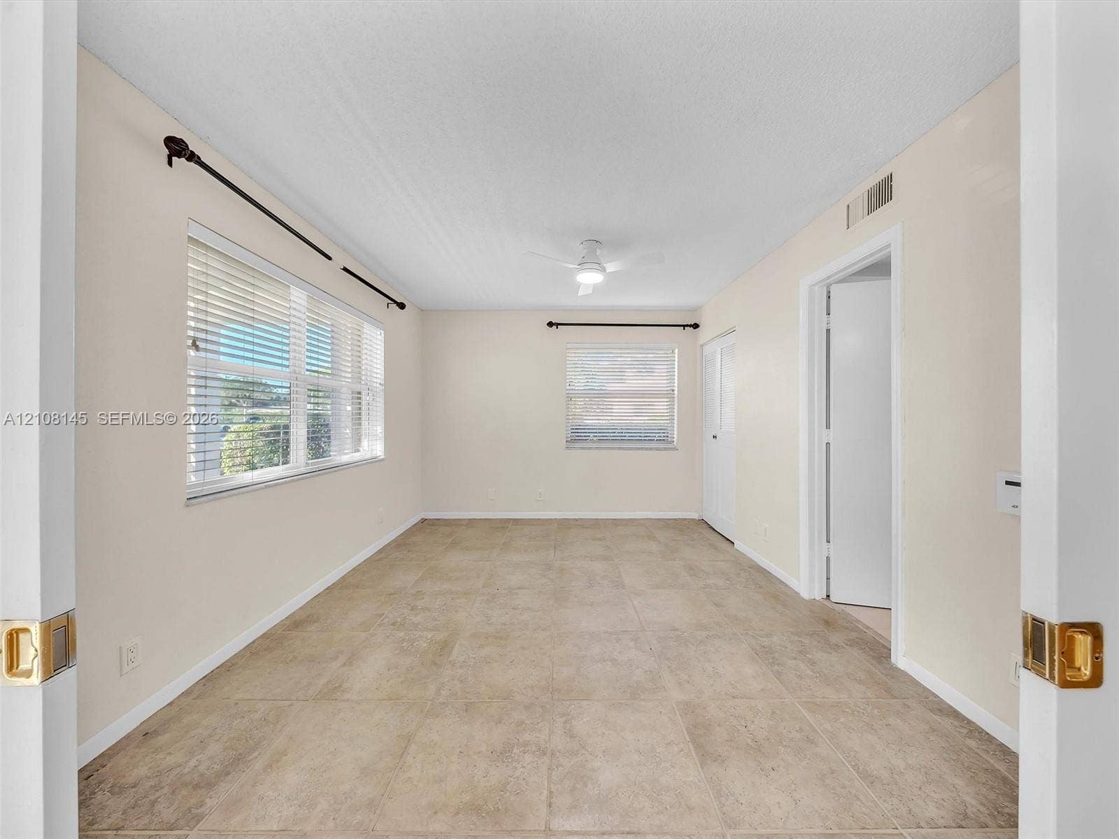 1020 Citrus Way, #101, Delray Beach, FL 33445 Neutral-toned room featuring large-format tile flooring, dual windows with horizontal blinds, a central ceiling fan with integrated lighting, and white interior doors