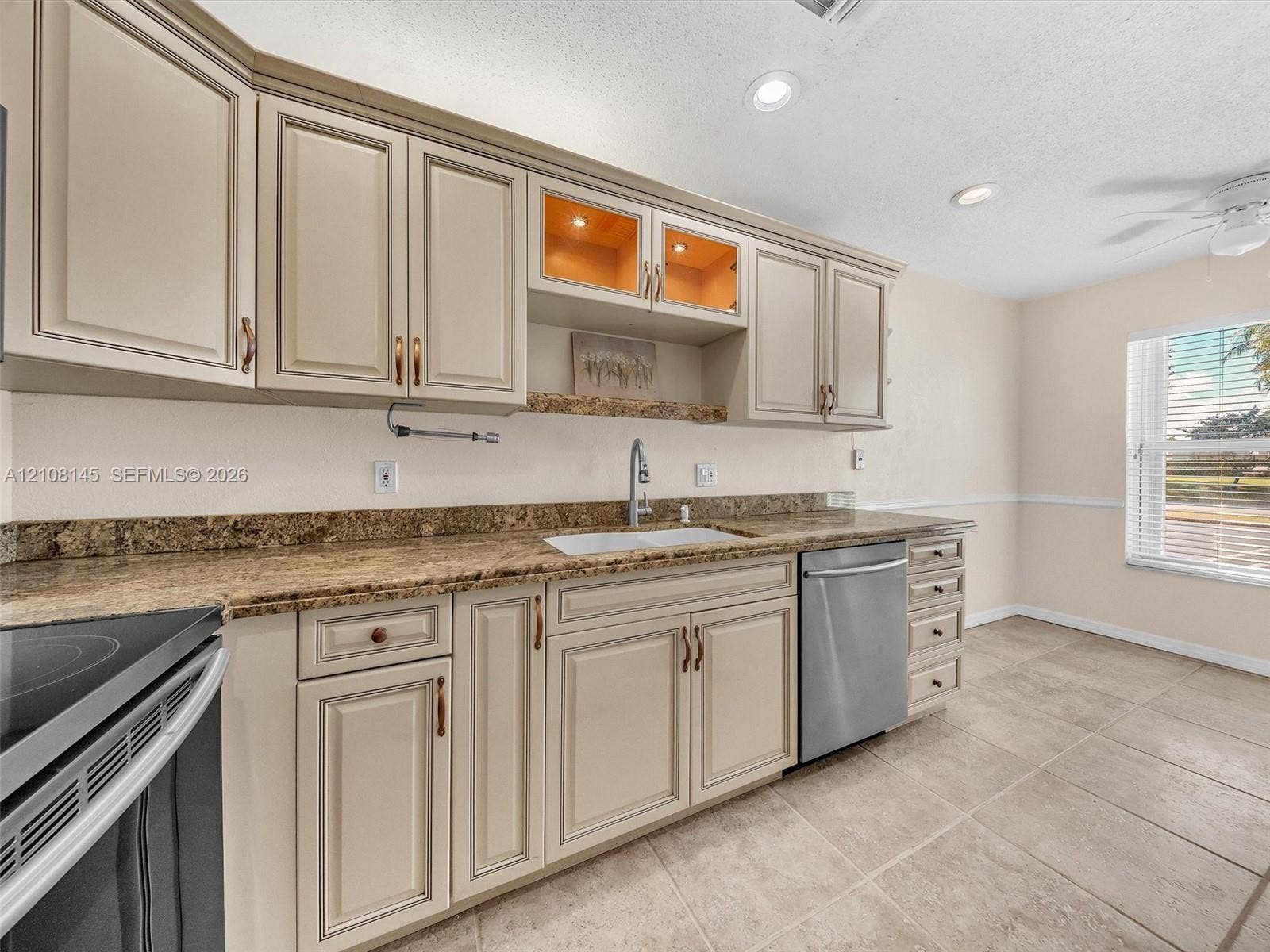 1020 Citrus Way, #101, Delray Beach, FL 33445 Kitchen featuring light-toned raised-panel cabinetry, stone-finish countertops, stainless steel dishwasher, integrated glass-front display shelving, and neutral tile flooring