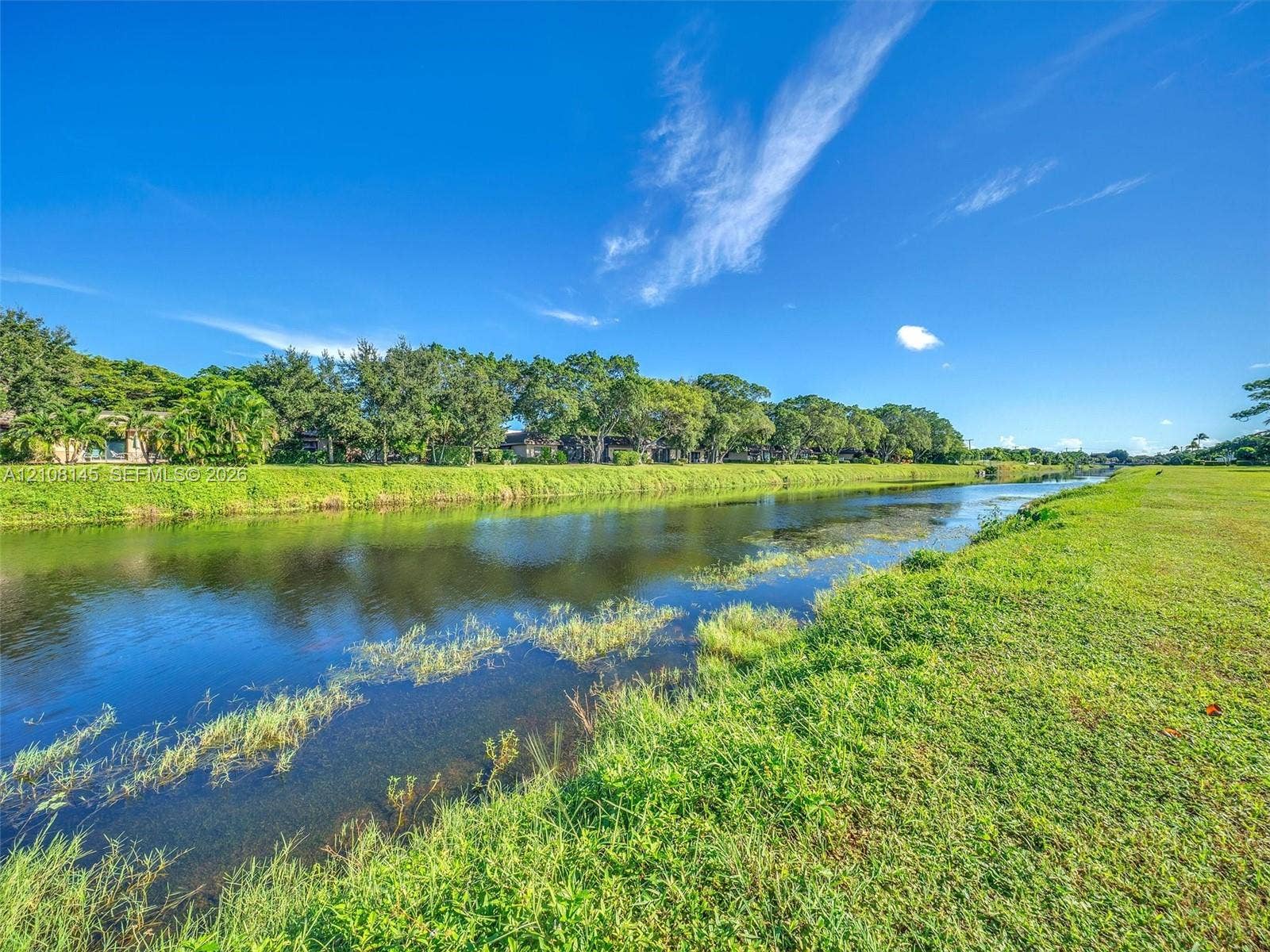 1020 Citrus Way, #101, Delray Beach, FL 33445 Waterfront property featuring a canal, expansive grassy lawn, and mature trees