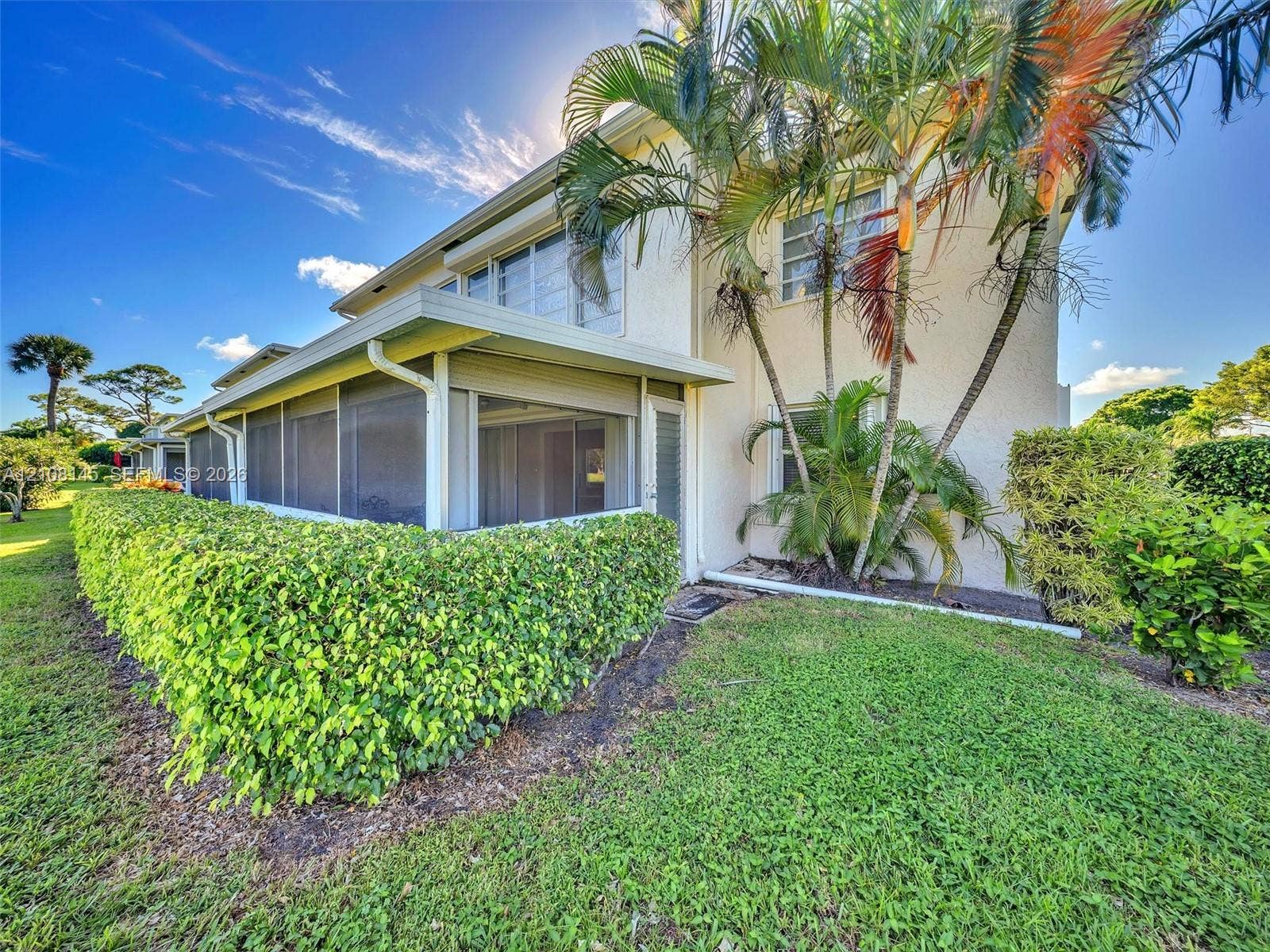 1020 Citrus Way, #101, Delray Beach, FL 33445 Stucco exterior featuring a screened-in ground level porch, mature palm trees, manicured hedges, and a grass lawn