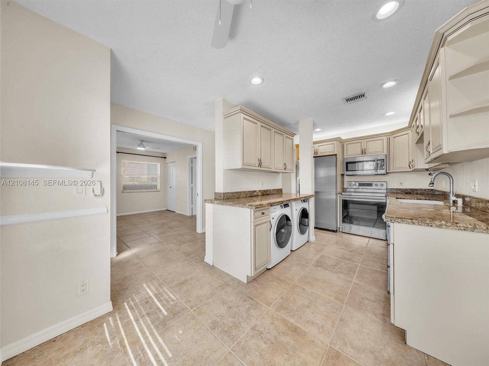 1020 Citrus Way, #101, Delray Beach, FL 33445 Kitchen featuring light-toned cabinetry, stone-finish countertops, stainless steel appliances, integrated laundry area, and tile flooring