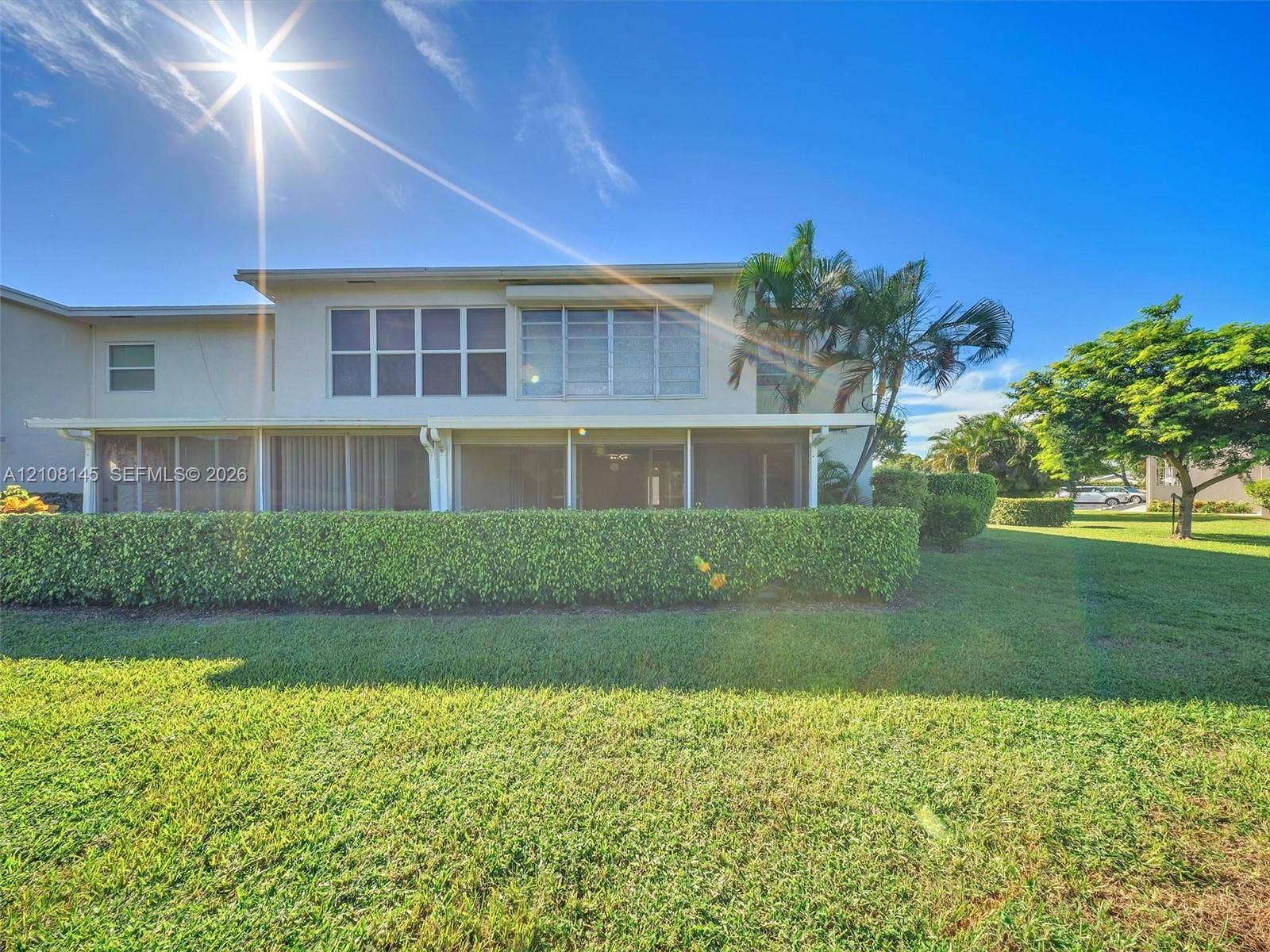 1020 Citrus Way, #101, Delray Beach, FL 33445 Two-story exterior featuring a screened-in ground-level patio, multi-pane windows, mature landscaping, and an expansive lawn