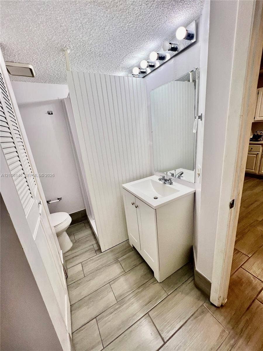 1258 S Military Trail, #813, Deerfield Beach, Deerfield Beach, FL 33442 Bathroom featuring wood-finish tile flooring, a white vanity cabinet with an integrated basin, a wall-mounted mirror, and beadboard wall paneling