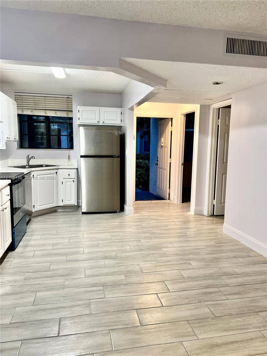 1258 S Military Trail, #813, Deerfield Beach, Deerfield Beach, FL 33442 Kitchen featuring wood-finish flooring, white cabinetry, stainless steel appliances, and a solid surface countertop