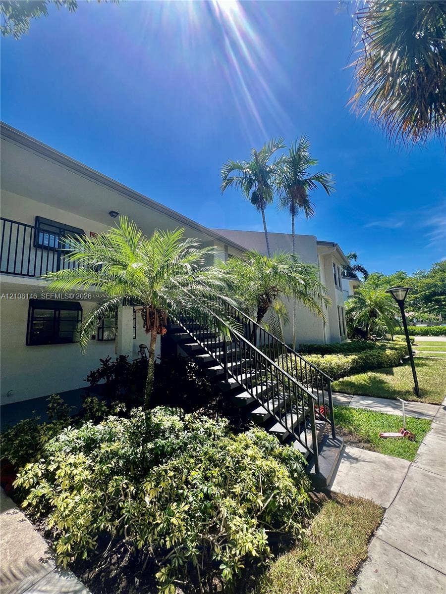 1258 S Military Trail, #813, Deerfield Beach, Deerfield Beach, FL 33442 Exterior of multi-story building featuring stucco siding, black metal staircase railings, balcony, and mature palm landscaping