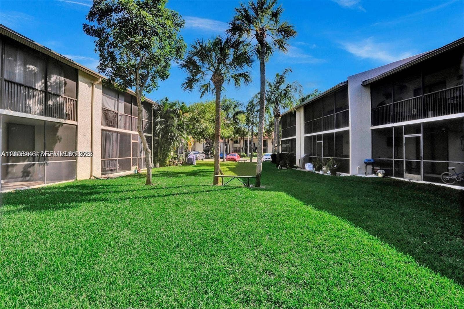 1258 S Military Trail, #813, Deerfield Beach, Deerfield Beach, FL 33442 Expansive central courtyard featuring a manicured lawn, mature palm trees, multi-story buildings with screened-in porches, and private balconies