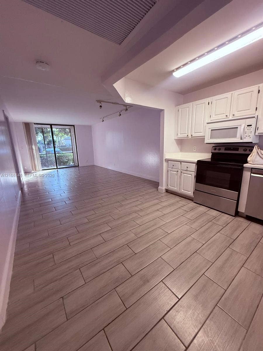 1258 S Military Trail, #813, Deerfield Beach, Deerfield Beach, FL 33442 Kitchen featuring white cabinetry, stainless steel appliances, and wood-finish tile flooring, complemented by sliding glass doors and track lighting