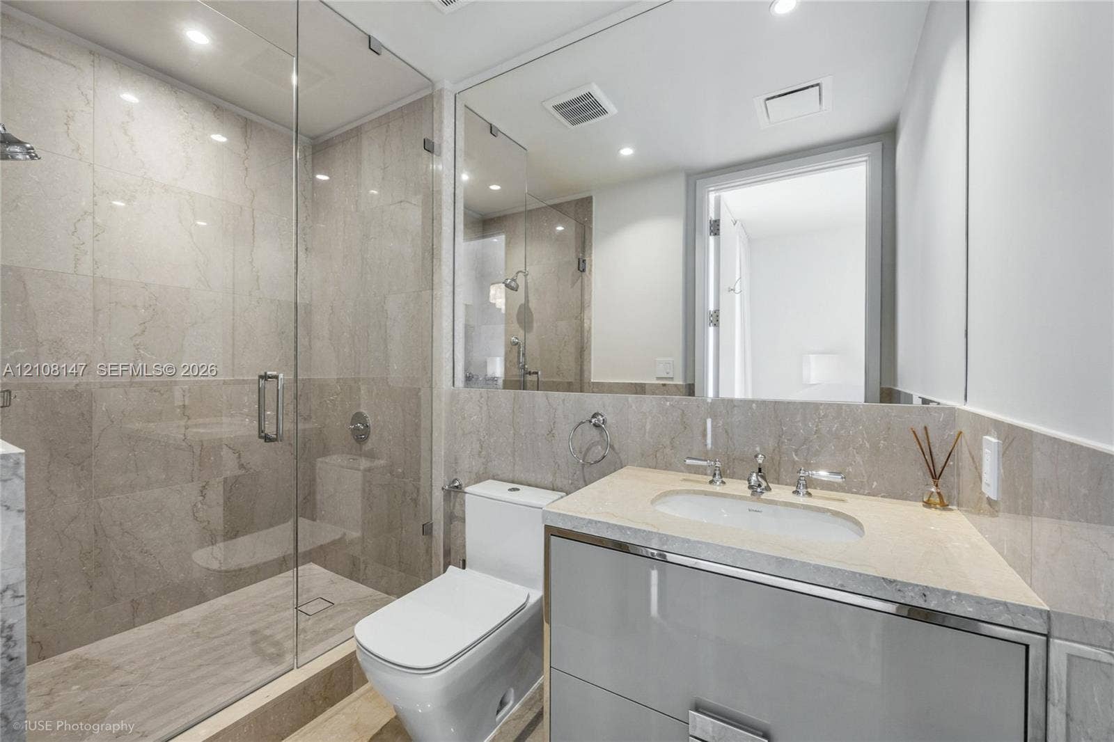 Glass-enclosed walk-in shower with floor-to-ceiling tile, high-gloss vanity with stone countertop, undermount sink, and full-width wall mirror