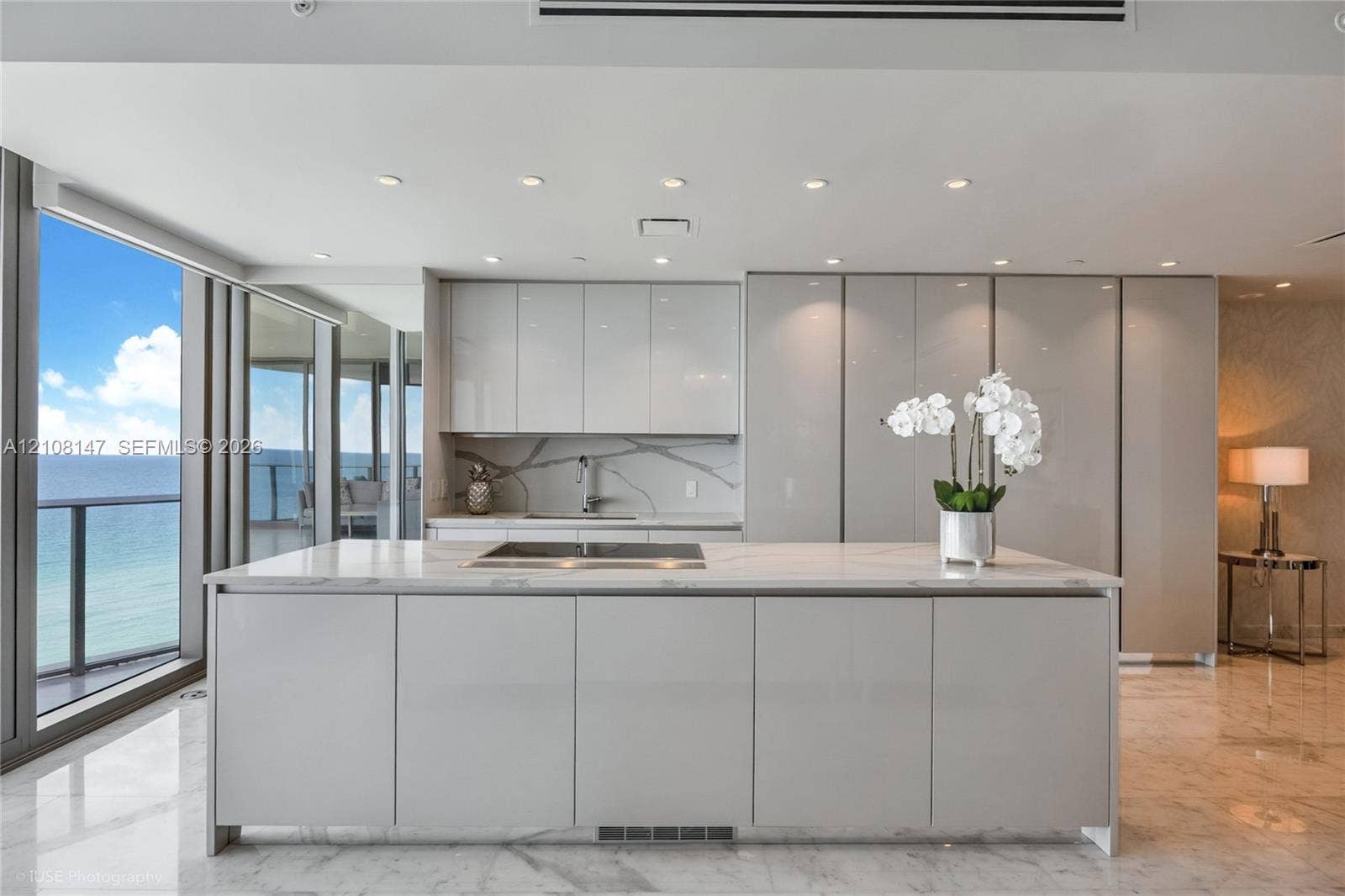 Kitchen featuring high-gloss cabinetry, stone-surface island with integrated cooktop, matching stone backsplash, polished tile flooring, and floor-to-ceiling windows